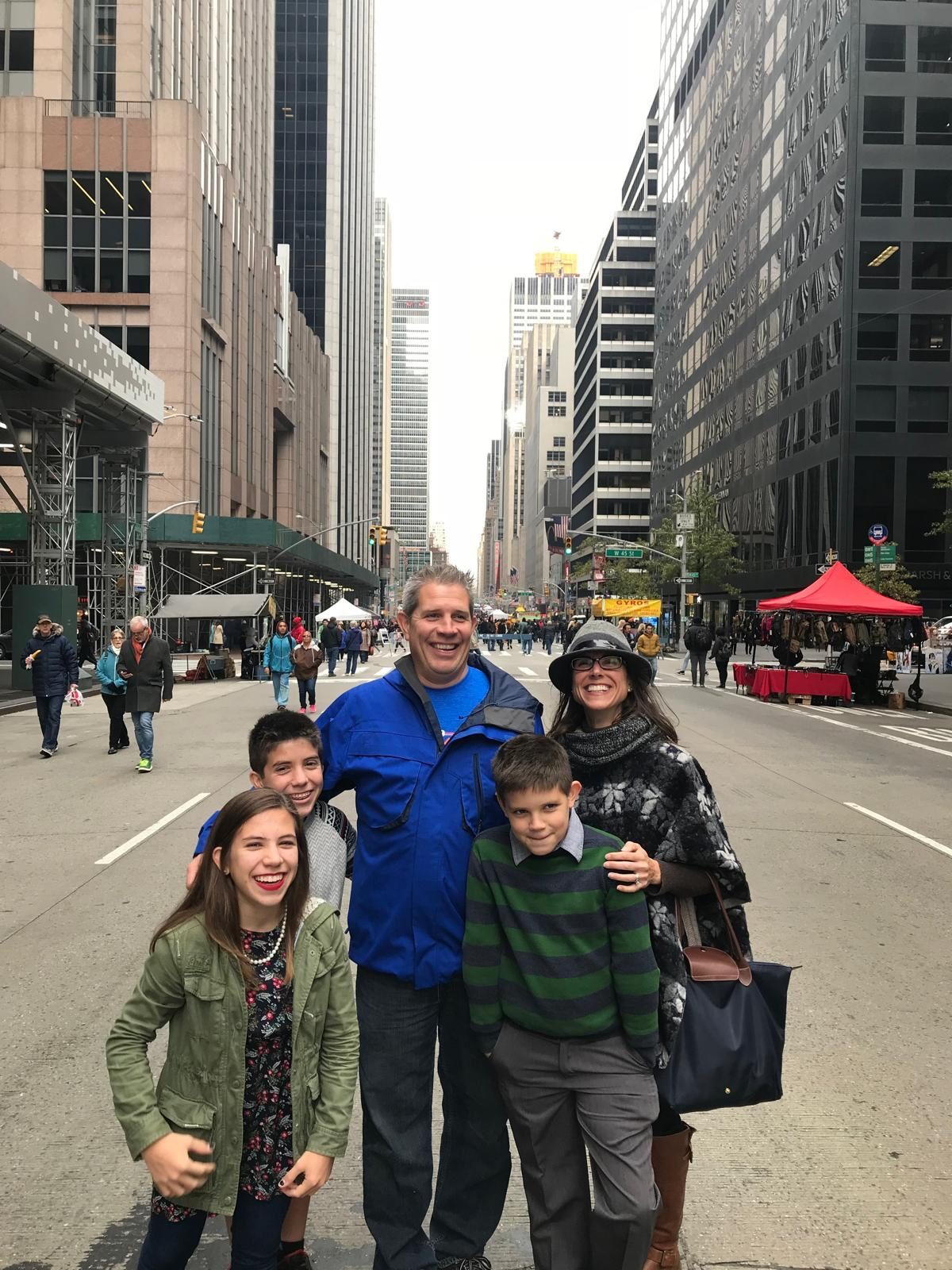 Aaron and his family standing together on a New York City avenue, skyscrapers rising on both sides.